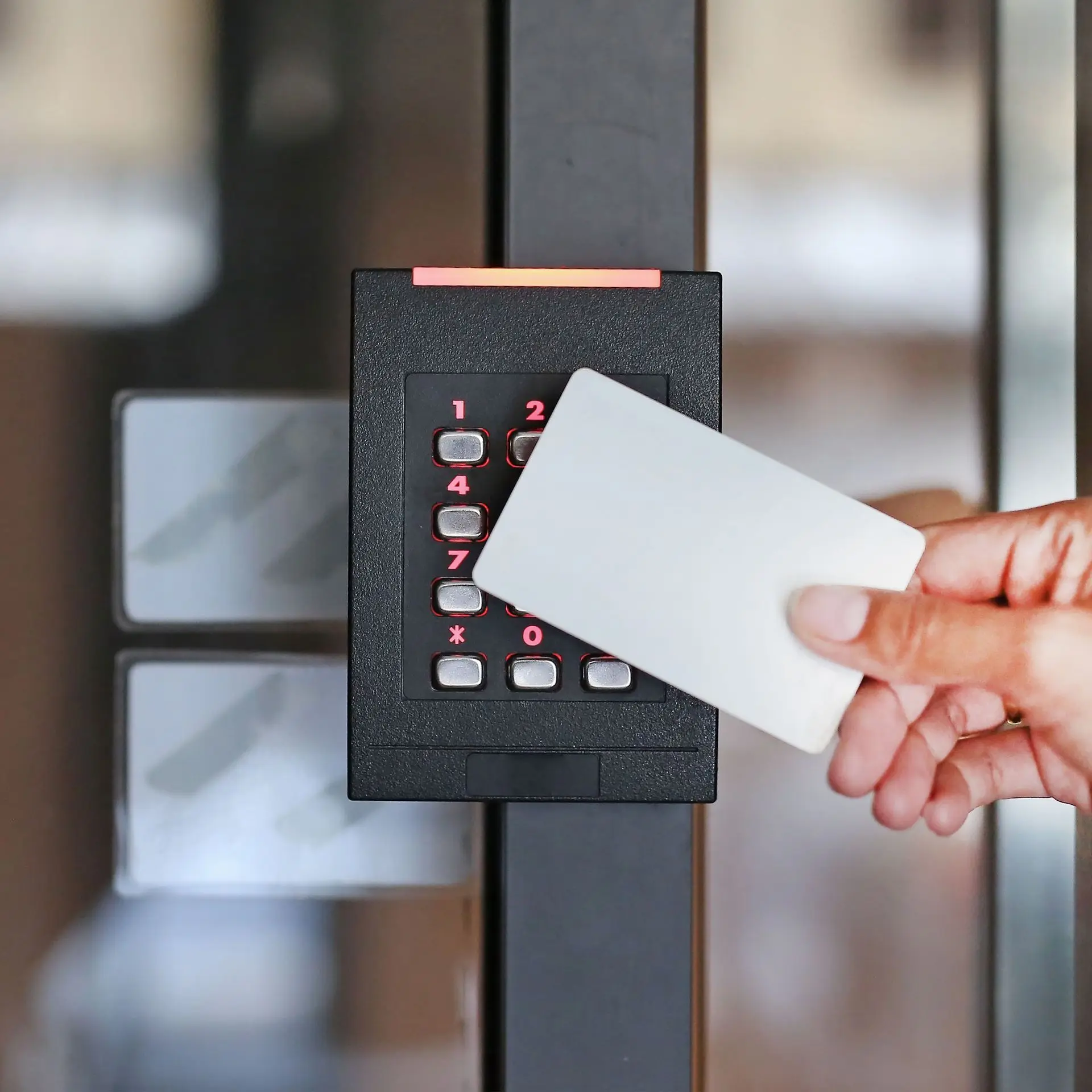 A hand holding an access card up to a keypad card reader beside a glass door
